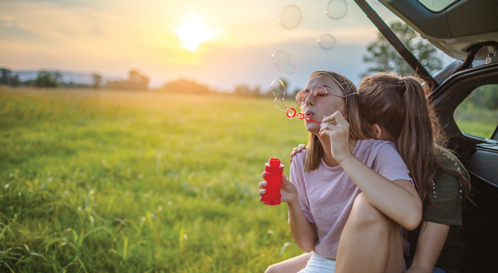 Image of two people sitting in their car blowing bubbles. 