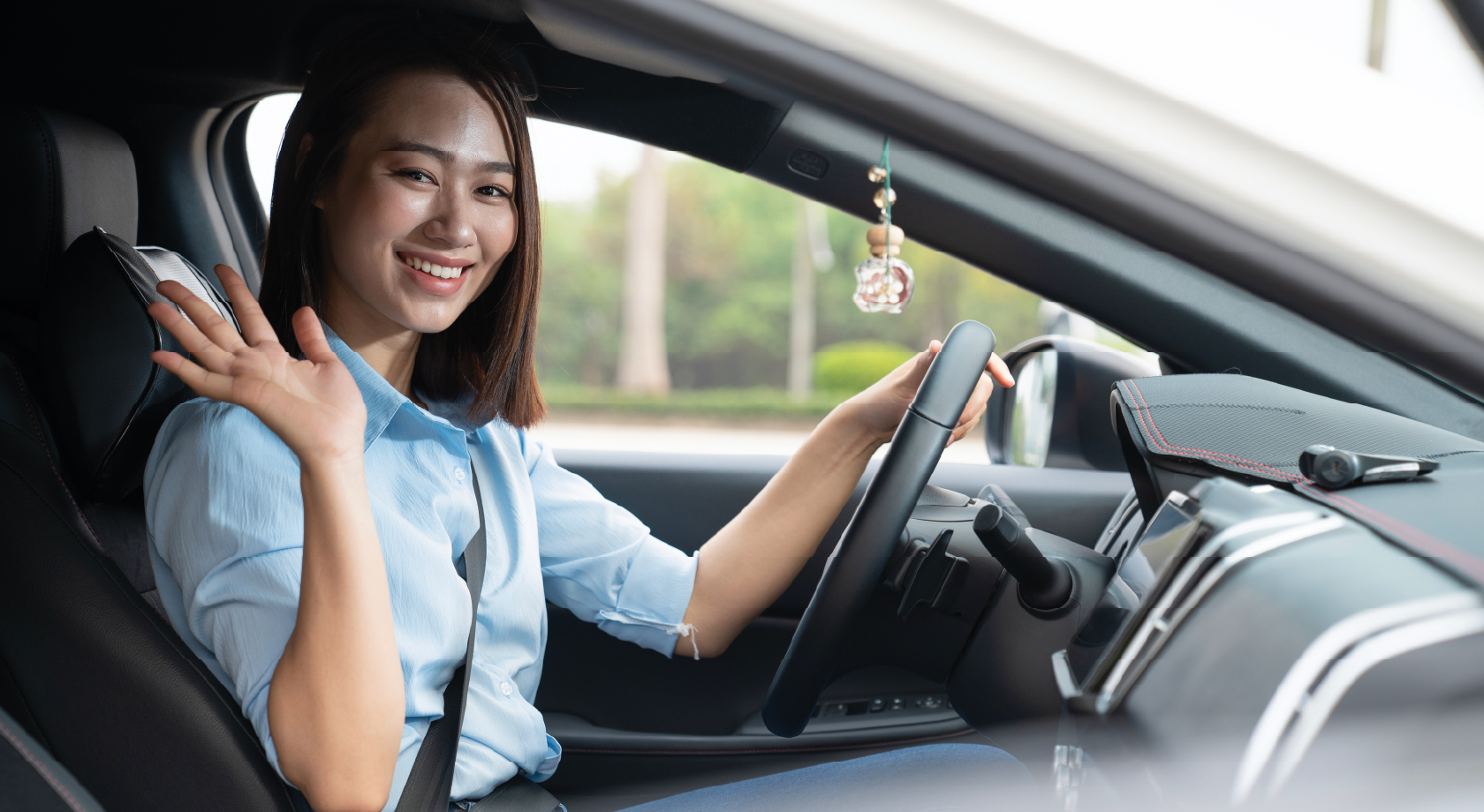 Woman in front seat smiling and waving while holding steering wheel