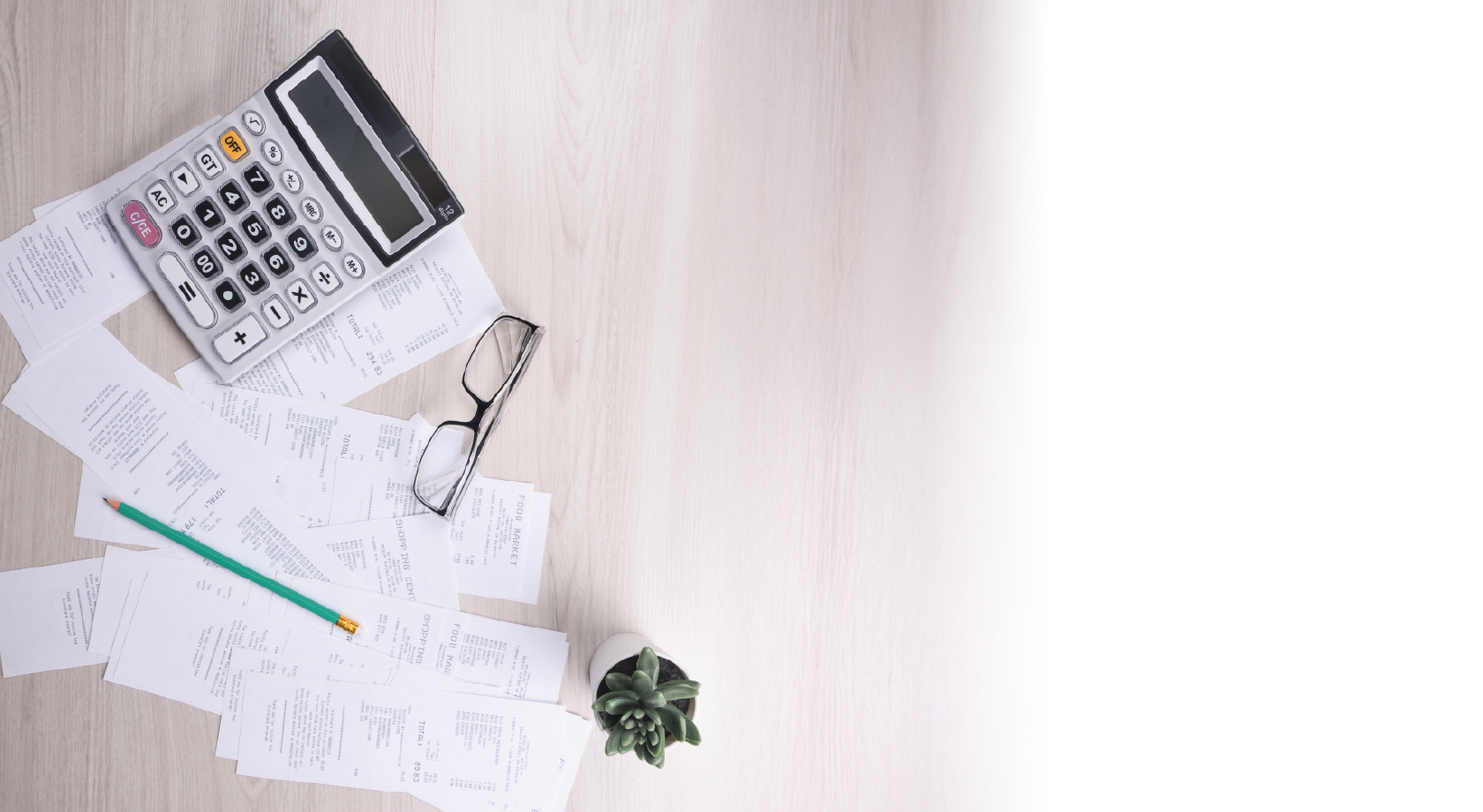 Papers and calculator scattered on desk with plant. 